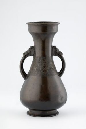  A dark brown, possibly metal or glazed ceramic vase with a footed base, swollen body, tapered and flared neck, and two curved ornate handles against a white background.