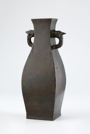  A tall, patinated bronze vase with angular sides and loop-style handles, set against a light background.