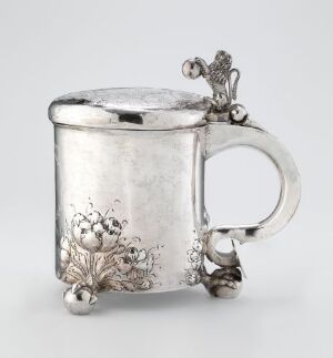  A silver drinking jug titled "Drikkekanne" by Jørgen Pedersen, with a smooth, polished surface and detailed engraved floral decoration near the base. It features a curved handle with a decorative attachment, a hinged lid topped with a small decorative figure, and three spherical feet. The craftsmanship reflects traditional silverworking techniques and artistic design.