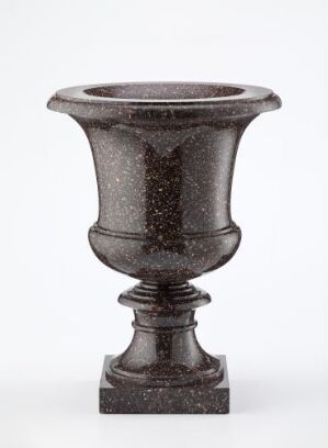  An urn-shaped, charcoal grey vase with a textured, speckled finish, resting on a square base, against a neutral background.