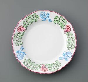  A round porcelain plate by Porsgrunds Porselænsfabrik AS with a white center and a hand-painted decorative border featuring green leaves, red berries, and blue flourishes around the rim.