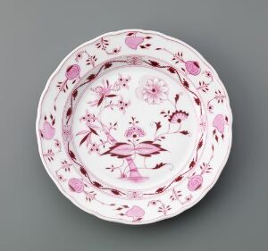  A decorative round plate with scalloped edges featuring a monochromatic floral pattern in shades of pink against a neutral grey background.