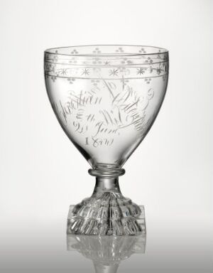  A clear glass goblet with a wide rim and a short stem, featuring intricate etched designs and faceted base, set against a white gradient background.