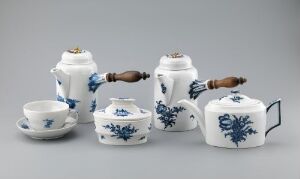  A set of white porcelain tableware titled "Blå blomst" by Den kgl. Porcelainsfabrik, including a cup and saucer, a teapot with a wooden handle, a sugar bowl with wooden handle, and a creamer, all decorated with a hand-painted cobalt blue floral underglaze pattern on a light gray background.