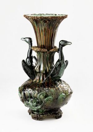  An ornate vase with a flared top and bulbous base in iridescent shades of emerald green and brown, featuring animal-like figures as handles.