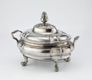  Antique silver-colored oval serving dish or soup tureen with decorative feet and handles, featuring a contoured lid with a pear-shaped finial, displayed against a light gray background.