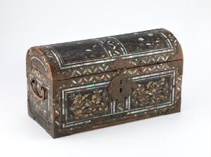  An ornate wooden chest with a curved top, adorned with geometric and floral inlays in a contrasting light color, sits against a light gray background.