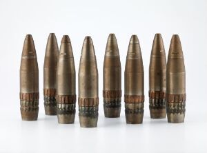  Seven 88mm artillery shells, designed by Raufoss Ammunitions Factories, aligned horizontally. They feature a polished copper body with a darker steel base and intricate bands, showcasing industrial design against a plain white background.