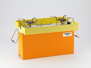  A portable Primus 2222 gas stove designed by Rolf Häggbom, featuring a bright orange base, yellow protective wind guards for the burners, and the brand label across the front. The design is simple and functional, indicative of Scandinavian industrial design with a focus on practicality and bright, inviting colors.