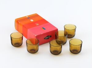  "Snapsilasi 5023" by Kaj Franck, featuring a bright orange rectangular cardboard box with a keyhole graphic surrounded by six amber-colored shot glasses, evoking a sense of modern, functional elegance in glassware design.