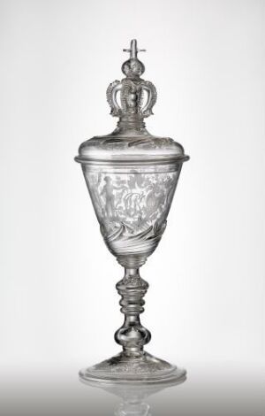  An intricately designed transparent glass goblet with a finial, crown-like structure on the cover, and an engraved floral pattern throughout. The goblet has a helical stem and a firm, decorative base, displayed against a soft, neutral background.