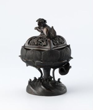  A dark bronze or black metal sculptural object featuring a spherical element with textured segments, supported by three ornately curved legs on a circular base. A small human-like figure sits contemplatively atop the sphere, adding an artistic and possibly symbolic element to the piece.