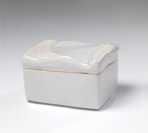 
 A small, rectangular, creamy white ceramic box with a slightly indented lid, placed at an angle on a plain background with soft shadows indicating its three-dimensional form. Artist name and title are unknown.