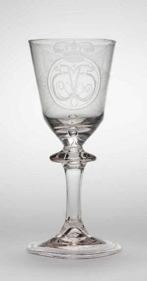  A clear glass goblet with an embossed monogram design in the bowl, an intricate stem with multiple shaped elements, and a flared base, all set against a light grey background.