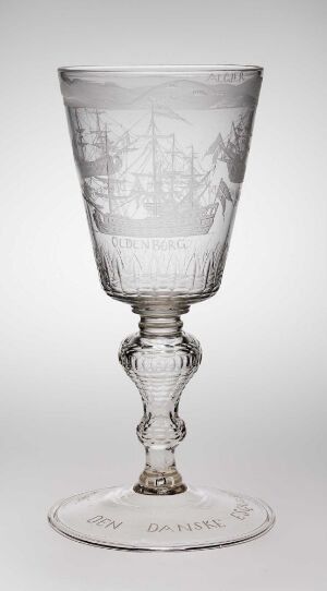 
 An intricate clear glass goblet with detailed engravings on its bowl, stem, and foot, set against a light grayish-white gradient background.