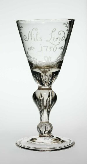  An elegant, transparent glass goblet with a wide mouth and narrow base, featuring ornate script and the date "1750" etched on the upper section, and a sculpted stem with a bulbous design, set against a gradient background fading from white to grey.