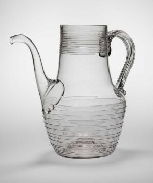  A clear glass pitcher with horizontal ridges and an elegantly curved spout and handle, set against a light gray background.