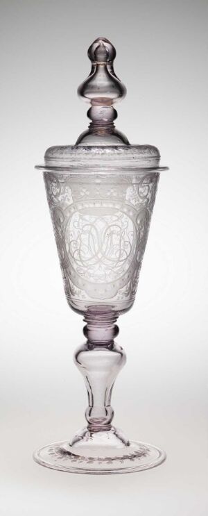  A tall and clear glass goblet with a detailed emblem embossed on the cup and a finial-topped lid, set against a white background.