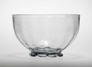  A transparent glass bowl with a simple design and smooth surface, standing on three small, round feet, set against a neutral background.