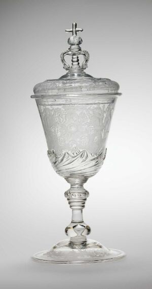  A tall, ornately etched transparent glass goblet with a flared base, spherical stem elements, and a lid topped with a cross, set against a light grey background.