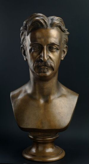  A bronze bust of Oluf Tostrup on a dark background, created by Drammens Jernstøberi, showcasing detailed hair, mustache, and expressive eyes, with a reflective bronze finish on a classical pedestal.