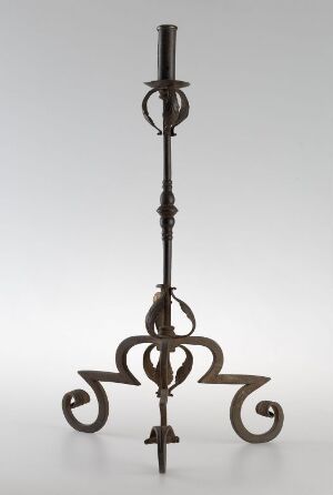  An antique metal candlestick with a twisted central post and ornate, curvilinear legs or supports, set against a light gray background.