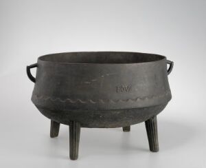  An antique three-legged metal cauldron with a wide opening, featuring simple zigzag patterns and horizontal handles, set against a gradient gray-to-white background.