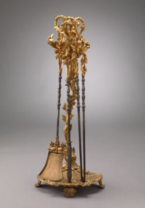  An ornate, tall golden pedestal with a bell-shaped base and four dark, slender rods extending upward, converging at a cluster of intricate golden forms, set against a neutral grey background.