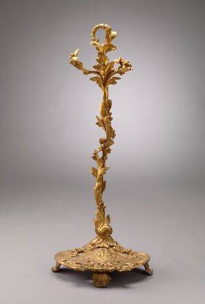  An intricately designed gold-toned candlestick or decorative staff with a vine and leaf motif throughout, standing against a neutral grey background.