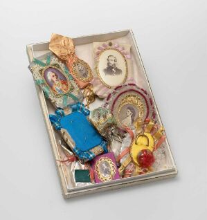  A curated assemblage of items within a metal tray includes a sepia portrait of a bearded gentleman, colorful paper items with decorative patterns, a golden watch, a small blue fabric-covered object, and a religious icon among other intricate personal objects.