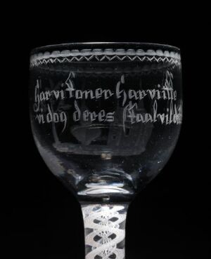  An ornate clear glass goblet with Scandinavian engraved text and decorative borders, set against a dark background, showcasing a monochromatic spectrum from translucent to gray shades.