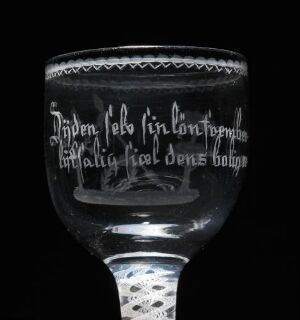  An antique wine glass with intricate etchings and script against a black background, showcasing a historically styled design with minimal color variation from greys to black.