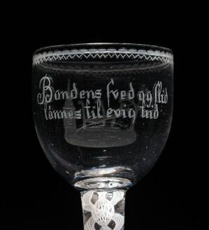  A historical goblet of dark smoky glass with frosted etchings, featuring Scandinavian text "til evig tid" and decorative patterns on the bowl, set against a black background.