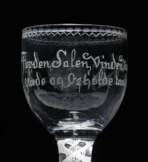  An antique smoky glass goblet with etched diamond patterns and scripted text against a dark background, featuring intricate designs on the stem and base.