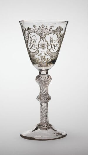  An ornate clear glass goblet with intricate engravings on the bowl and a twisted stem design, set against a light grey background.