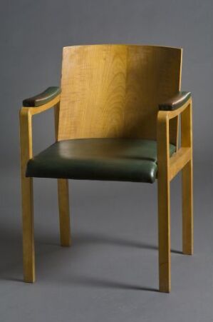  A modern chair with a curved wooden backrest featuring a golden hue and grain patterns, and a deep green upholstered seat, set against a plain gray background.