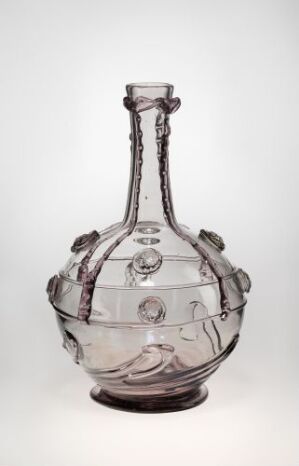  A colorless glass decanter with a rounded body and elongated neck, featuring raised linear patterns and circular indentations, complete with a twisted handle, displayed against a light neutral background. Artist name and title unknown.