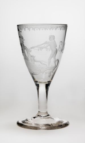  An elegant transparent glass goblet with intricate etchings of classical figures on the bowl, highlighted against a light background.