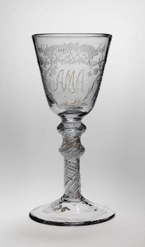 
 A clear glass goblet with an intricately designed stem and decorative etching, standing against a light gray to white gradient background.