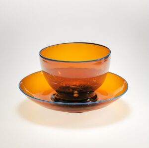  An amber-colored glass bowl sitting on a matching plate, both with a deep, brownish base, on a white background.