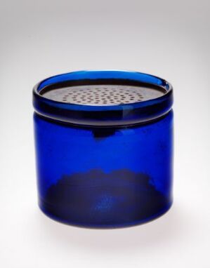  A cylindrical cobalt blue glass container with a metallic lid that has a pattern of holes on the top, set against a white background. Artist name and title are unknown.