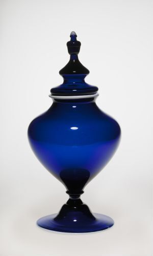  A glossy cobalt blue vase with a bulbous body, slender neck, and ornate lid stands against a light background, showcasing its simple elegance and rich color.