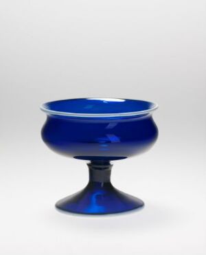  A cobalt blue glass bowl with a pedestal base placed against a plain white background. The bowl is translucent with a rich, deep blue color and a simple yet elegant design devoid of any additional decorations or embellishments. Artistname and title are unknown.