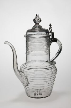  Black and white photograph of an ornate glass coffee pot with metal lid, handle, and band, featuring horizontal ridges on the glass for a textured look, displayed against a light background.