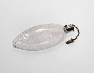  A transparent, faceted glass elliptical-shaped object with a metal cap and cork stopper attached by a chain, against a plain white background. Artist name and title are unknown.