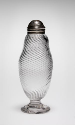  An elegant, clear glass container with a spiraled texture stands on a circular base, capped with a dark, rounded lid against a plain background. Artist and title unknown.