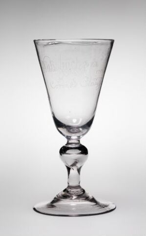  A clear glass goblet with a conical bowl, spherical knob on the stem, and flat circular base stands against a light grey background.