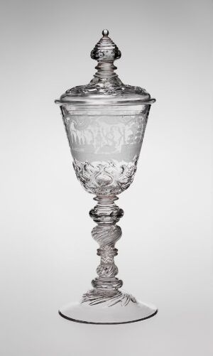  A transparent, intricately designed glass goblet with a spiral stem and lid, set against a neutral gray background.