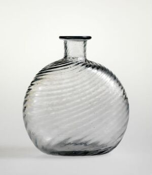  A clear glass vase with vertical ribbing creating a wave pattern, standing against a gradient background that shifts from light at the top to dark at the bottom. The vase has a flattened body and a narrow, flared neck.