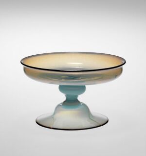  A delicate, opalescent glass compote with a shallow, iridescent bowl featuring creamy whites and soft blues that blend smoothly atop a short, stout stem and broad base set against a plain light grey background.